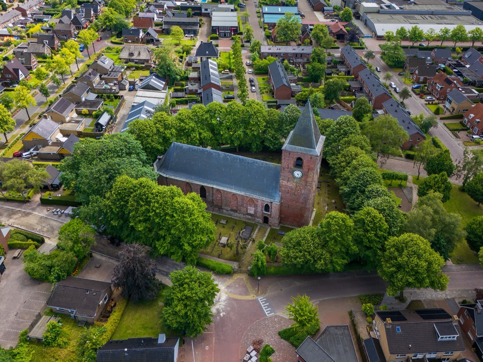 Oude kerk met toren tussen de bomen midden in een woonwijk