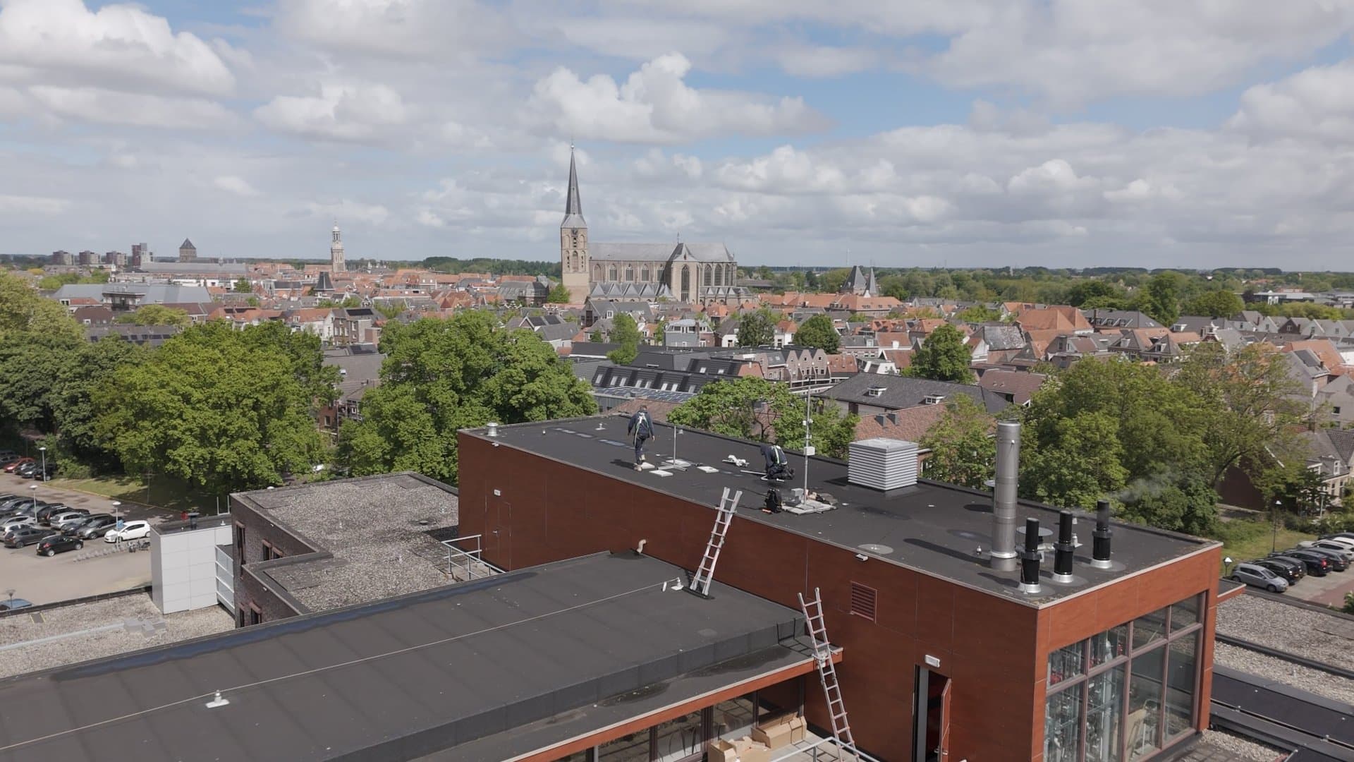 Monteurs aan het werk op een plat dak, met de stad en de kerk op de achtergrond